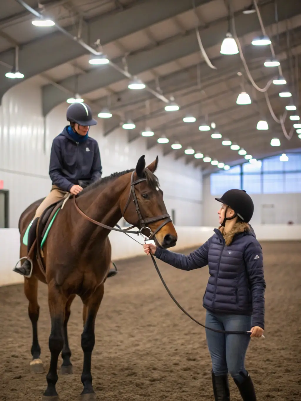 An experienced instructor guiding a group of riders through an advanced dressage training session in the indoor arena at ECURIE-MOULIN.